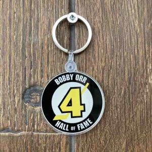 Round acrylic keychain with Bobby Orr Hall of Fame logo hanging in front of a wood backdrop.