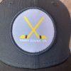 Grey patch embroidered onto a black baseball hat with two gold hockey sticks crossed, writing below the sticks reads "Parry Sound, ON"