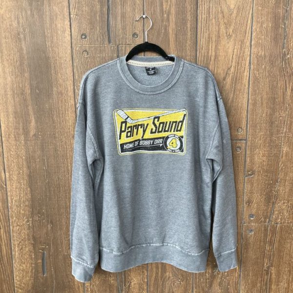 Grew washed sweatshirt hanging in front of a wood panel background. Sweatshirt has a screen-printed design of a billboard reading Parry Sound home of Bobby Orr.